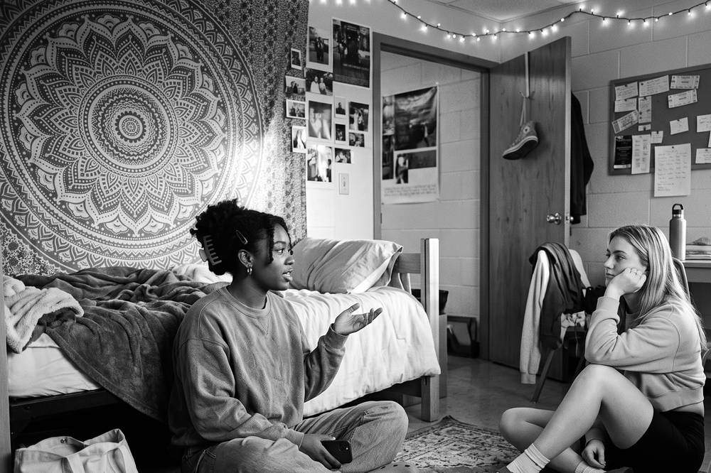 Two roommates at a dorm desk filling out the agreement together, snacks out, door propped open
