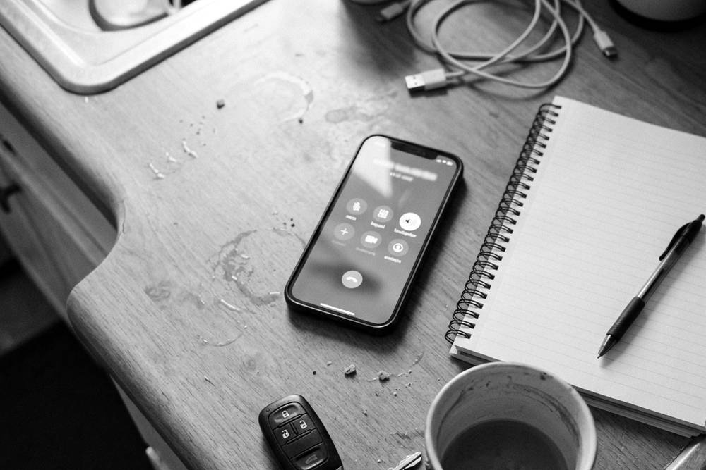 A parent's phone mid-call on the kitchen counter, a notepad beside it with two columns handwritten - 'VENT' and 'HELP', with a checkmark under VENT