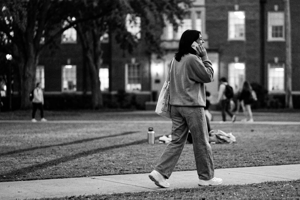 A student walking across campus at dusk, phone to ear, relaxed posture