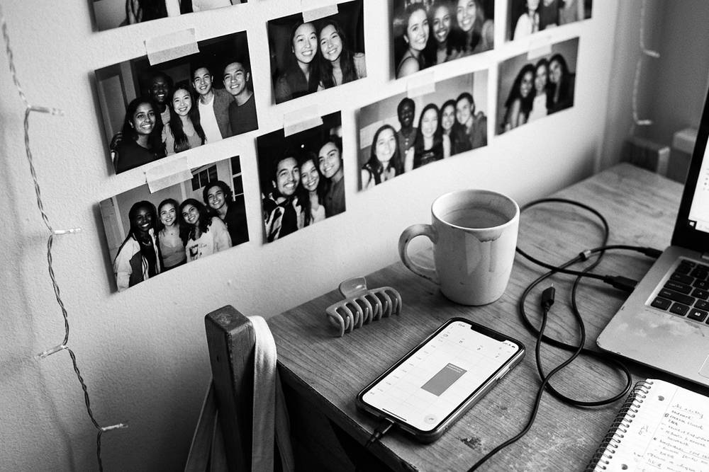 A phone on a dorm desk showing a recurring calendar entry, 'call home - Sunday 4pm,' with a laptop and a coffee cup beside it