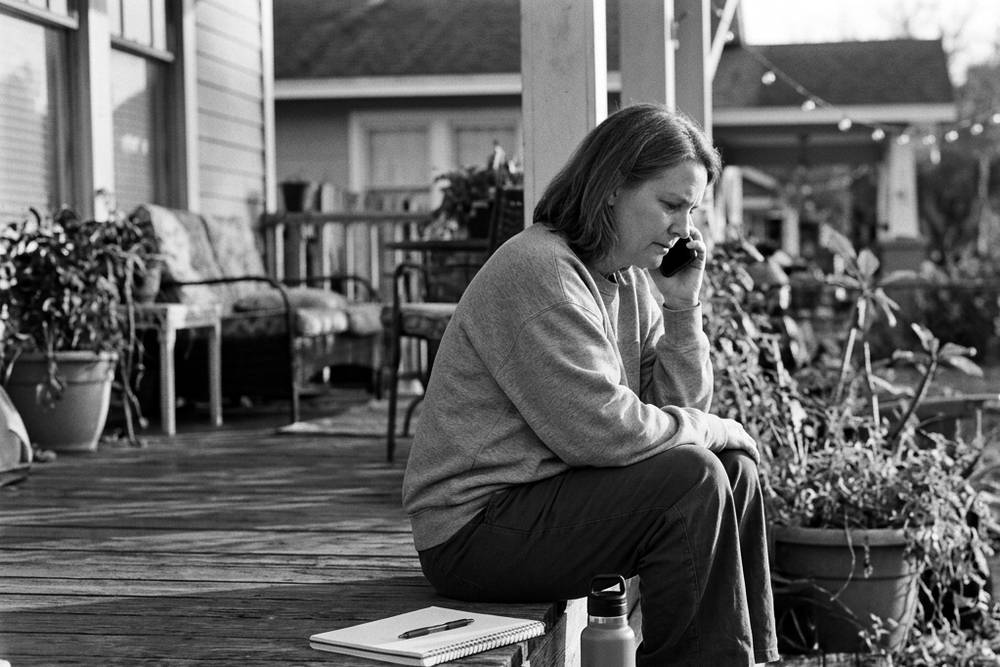A parent sitting on a porch step on the phone, listening rather than talking, notebook closed beside them