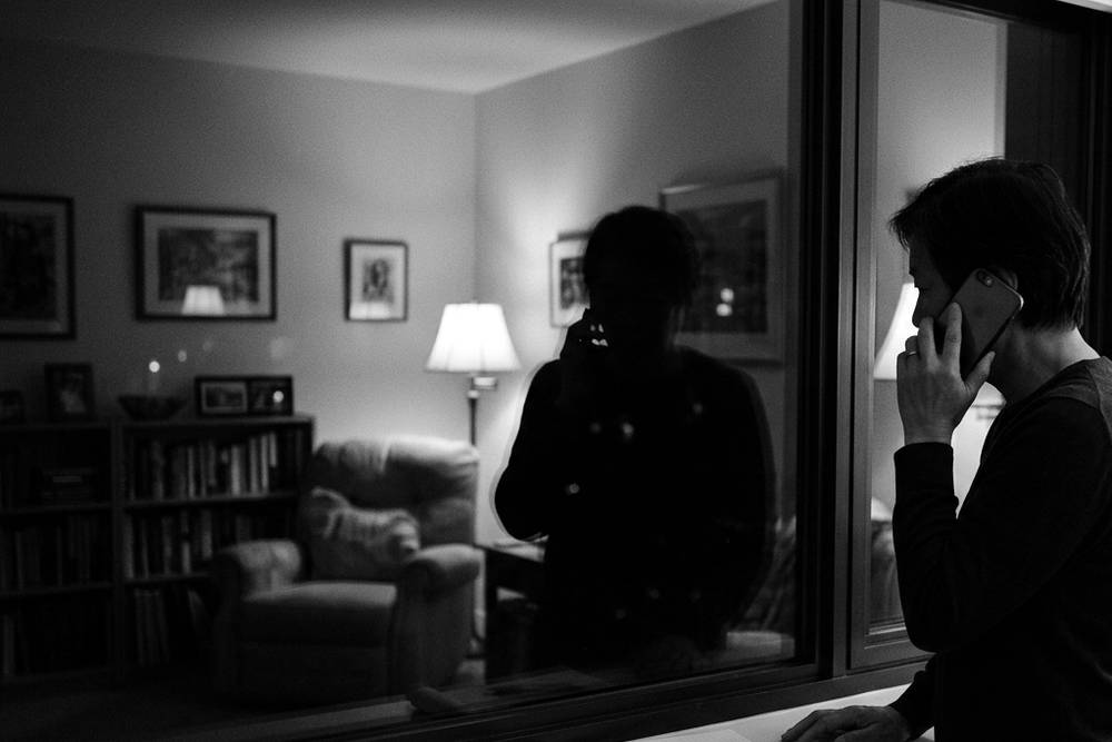 A parent on the phone, standing at a window at night, listening with a notepad they haven't written on