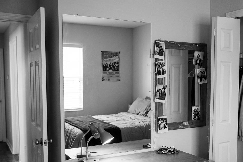 An empty bedroom with the bed made and the closet half full, morning light, door open